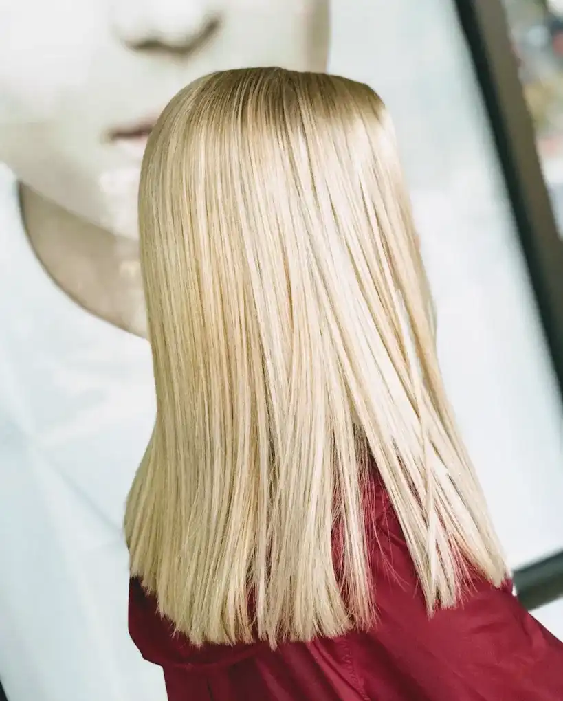 Sleek blond hair styled straight, person wearing a red outfit stands in front of an image.