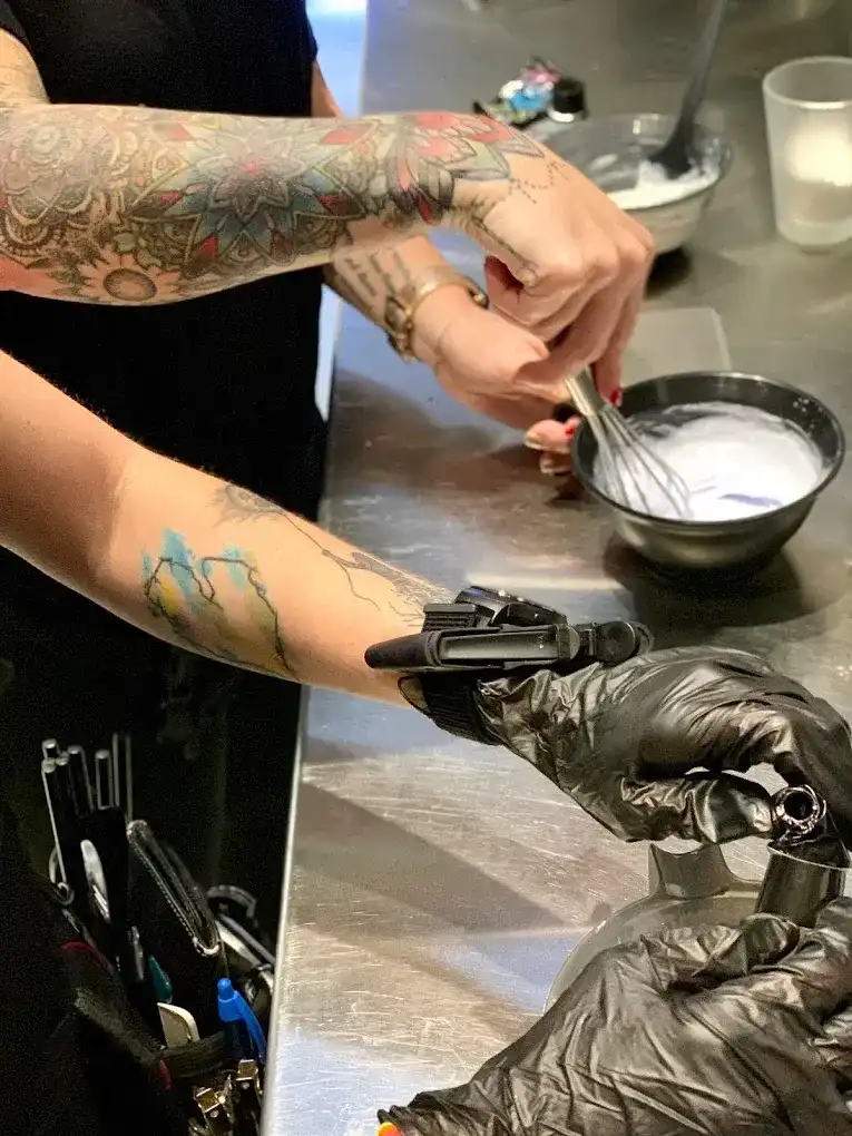 Tattooed person mixing hair color in a salon, showcasing tools and preparations.