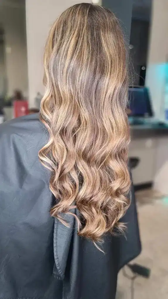 Wavy, long hair with light brown and blonde highlights in a salon setting.